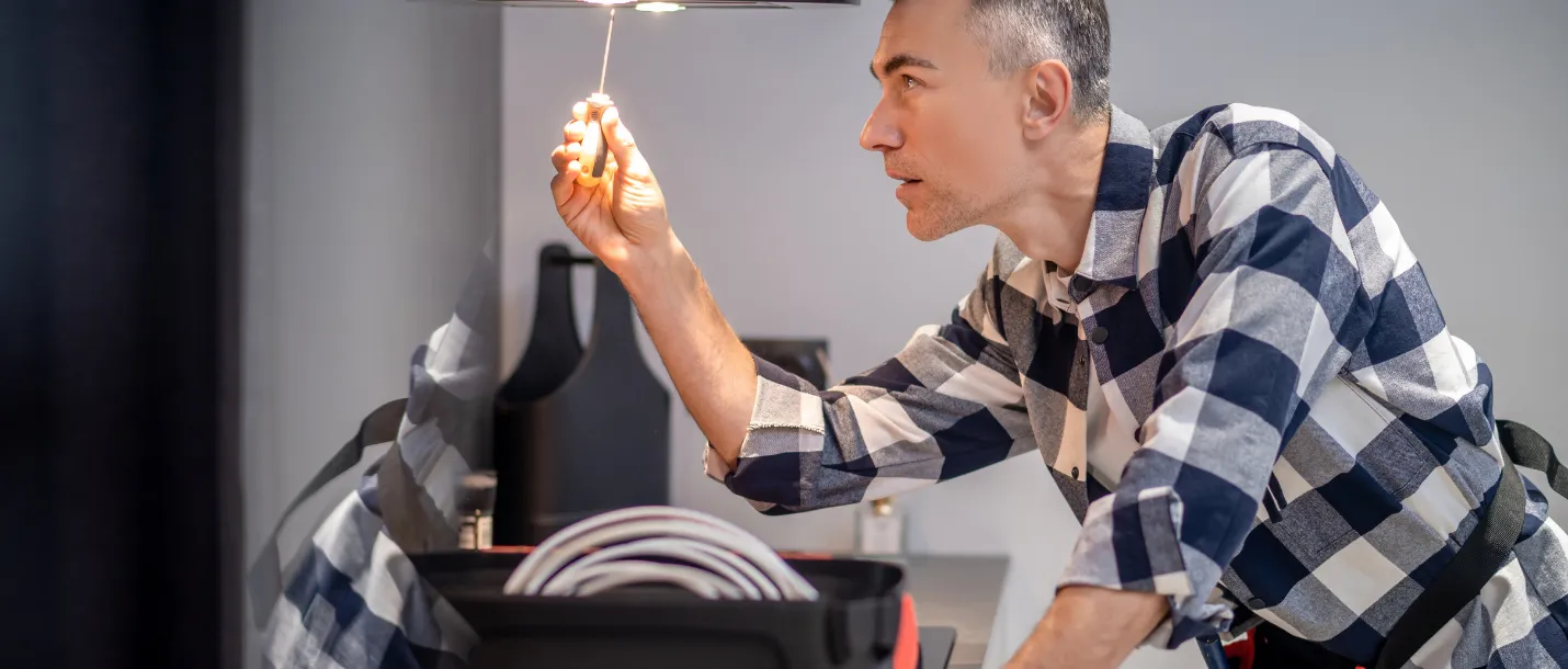 Handyman replacing ceiling light bulb during indoor home maintenance service